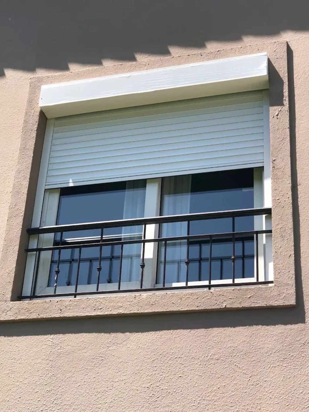 Cortina de enrollar parcialmente abierta sobre ventana con reja