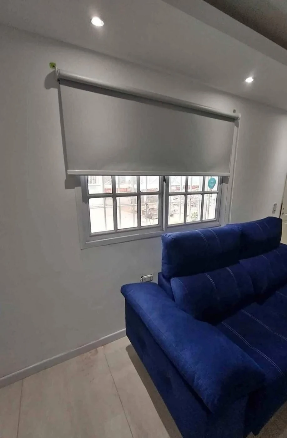 Cortina roller instalada sobre una ventana en un ambiente con sofá azul